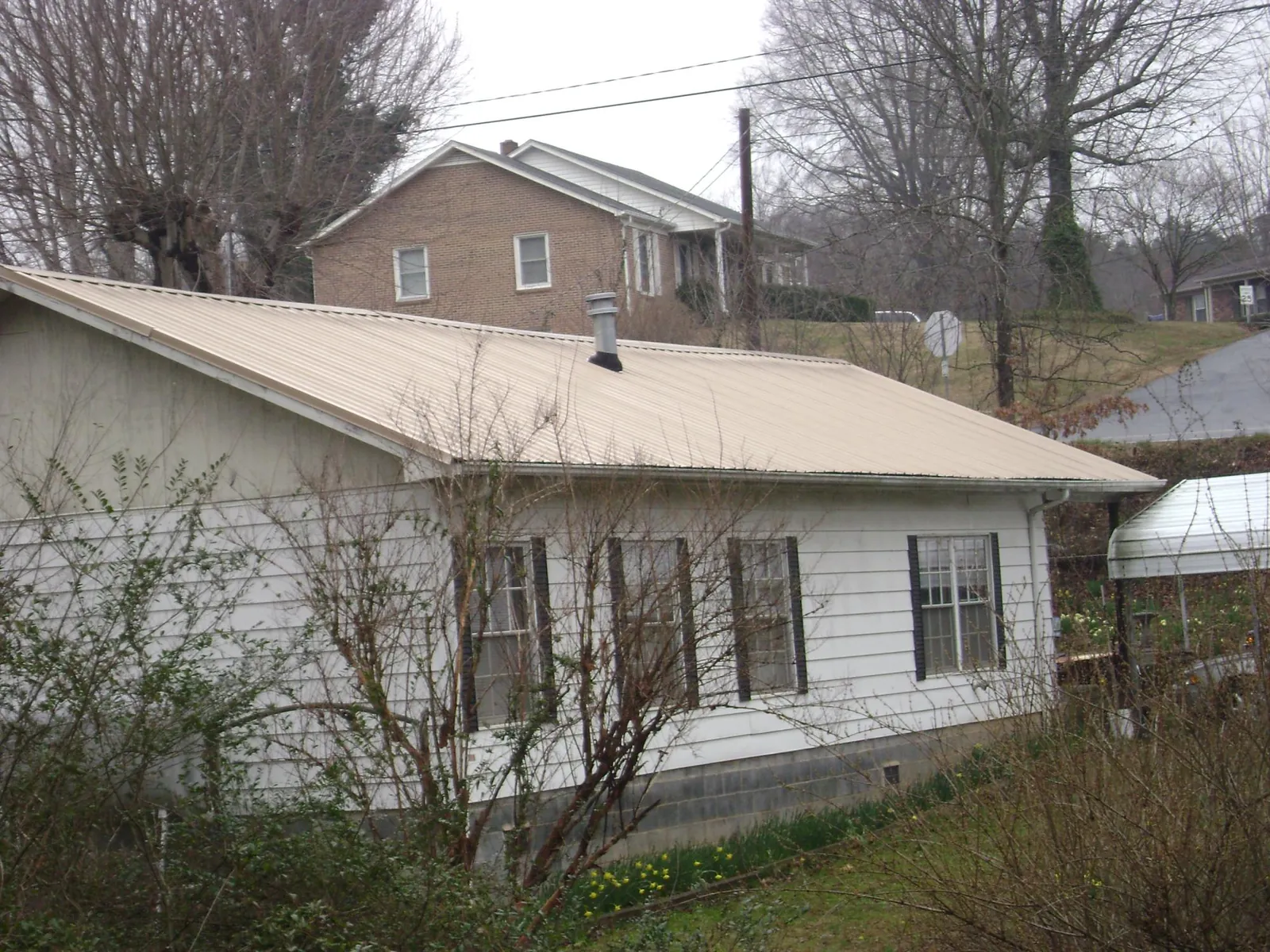 Tan metal roof on a white sided house set into a hillside — Commercial Roofing by Roofing Brothers in Garnett